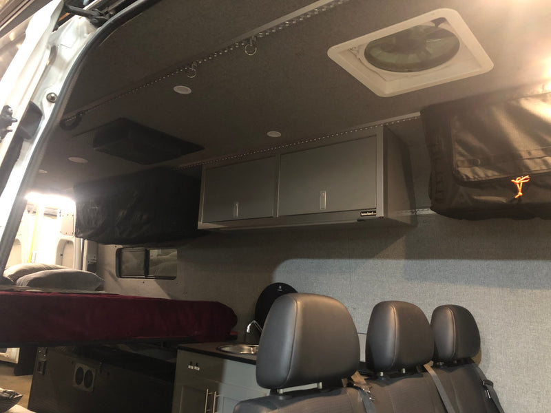 Spacious RV rental interior with a comfortable bed, kitchen area, overhead storage cabinets, and ceiling fan. — photo 8