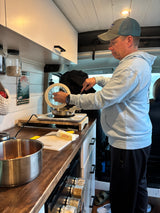 RV rental cooking: A man preps a meal in a compact, organized kitchen, featuring butter, spices, and travel decor.