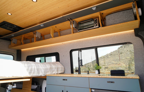 RV rental camper interior with bed, compact kitchen, toaster oven, and organized overhead storage, plus scenic window views.