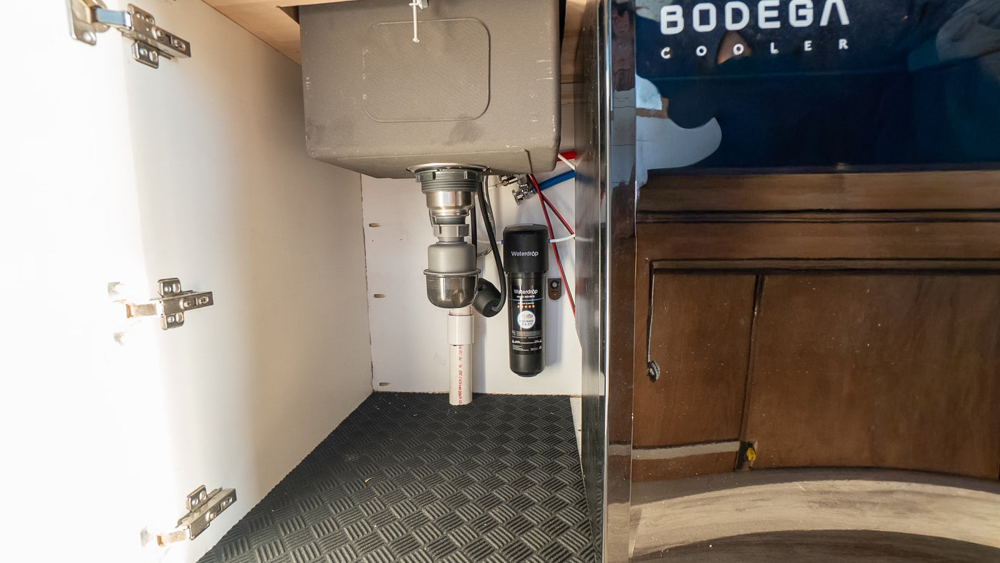 An RV rental's under-sink area, featuring plumbing, a Waterdrop filter, and a durable floor mat for a compact kitchen. — photo 20