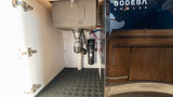 An RV rental's under-sink area, featuring plumbing, a Waterdrop filter, and a durable floor mat for a compact kitchen.
