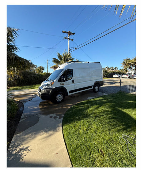 This white camper van, ready for RV rental adventures, is parked on a wet driveway on a sunny day.
