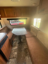 Inside an RV rental: a cozy dinette with patterned bench seating, table, and wood cabinets. Features durable flooring.