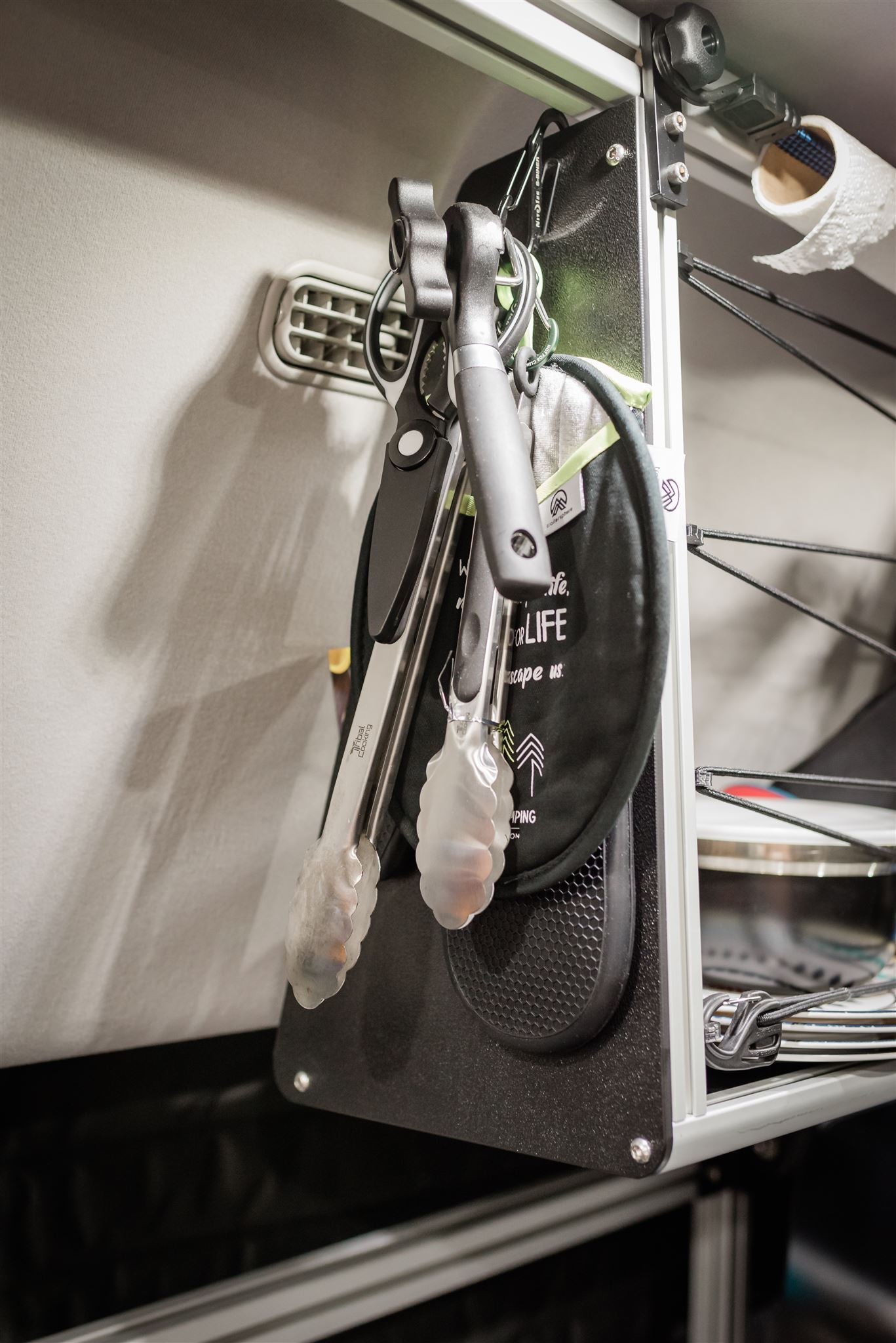 Organized RV rental kitchen featuring hanging cooking utensils, pot holder, and paper towels. Efficient camper storage for travel.