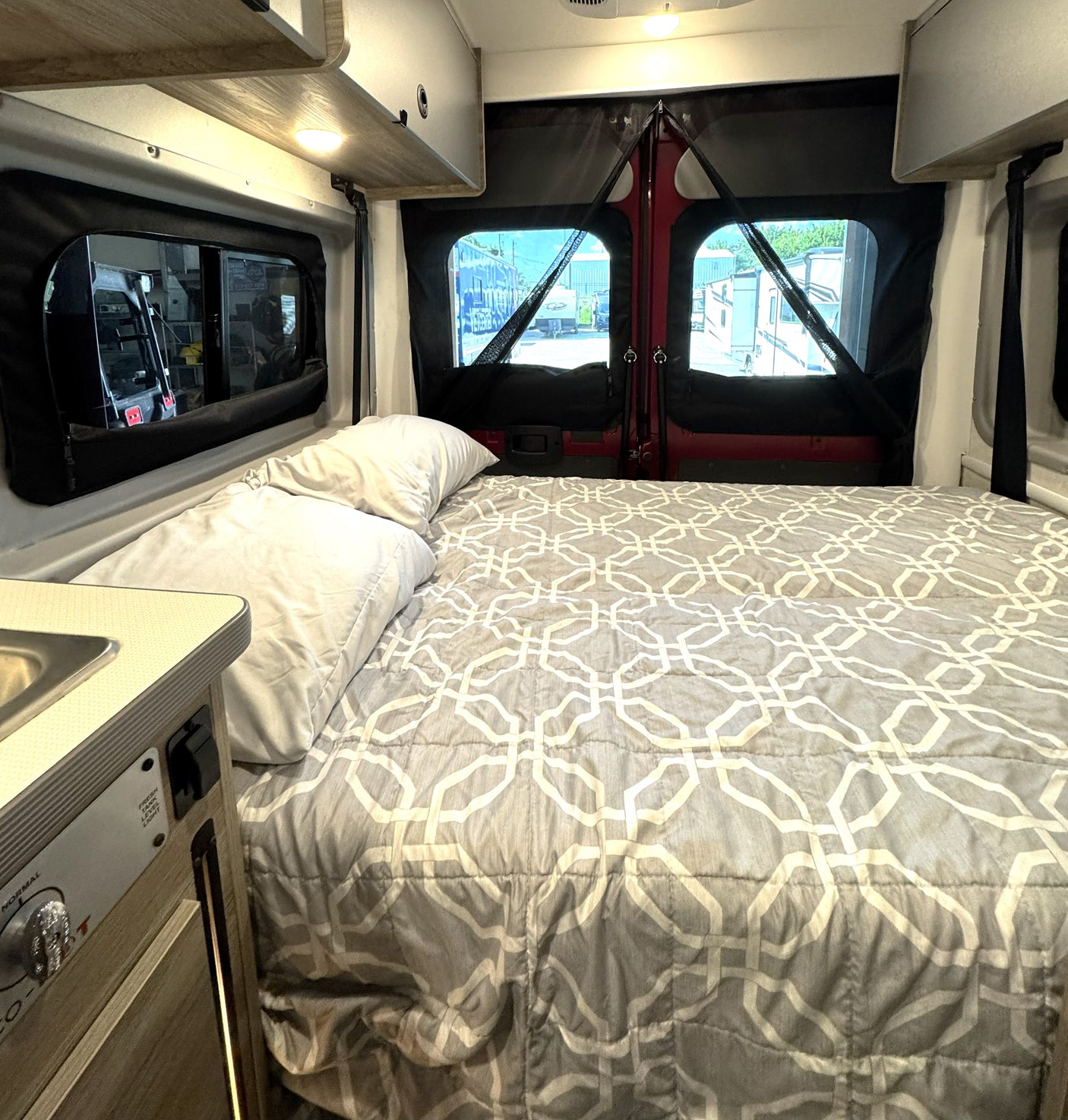 Cozy rv rental interior: bed with gray geometric comforter, pillows, and screened windows.