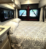 Cozy rv rental interior: bed with gray geometric comforter, pillows, and screened windows.