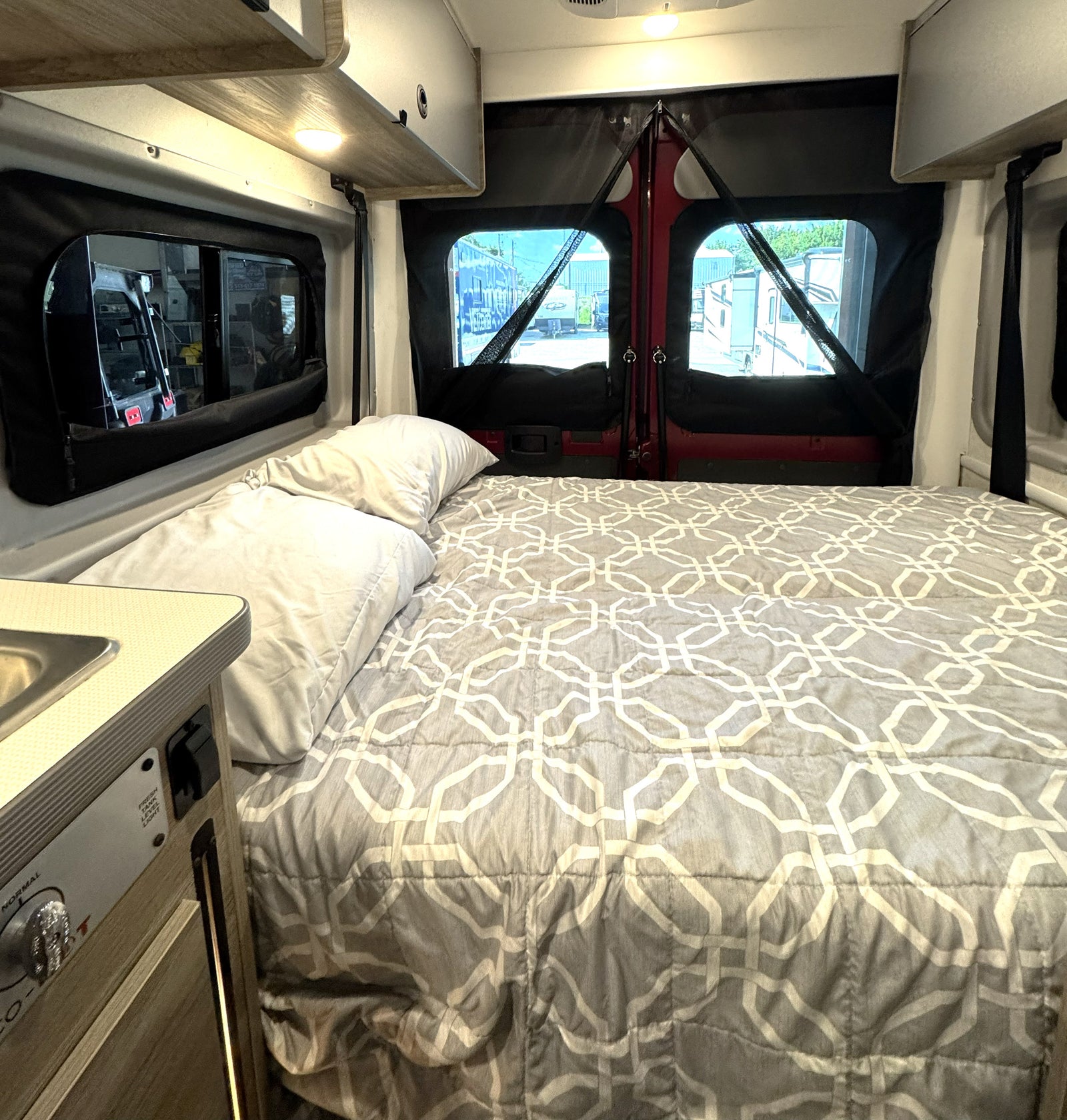 Cozy rv rental interior: bed with gray geometric comforter, pillows, and screened windows.