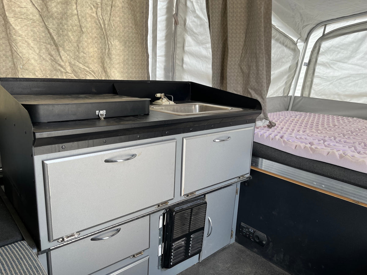 Interior of a pop-up camper RV rental: compact kitchen with a sink, storage cabinets, and a comfortable bed. — photo 6