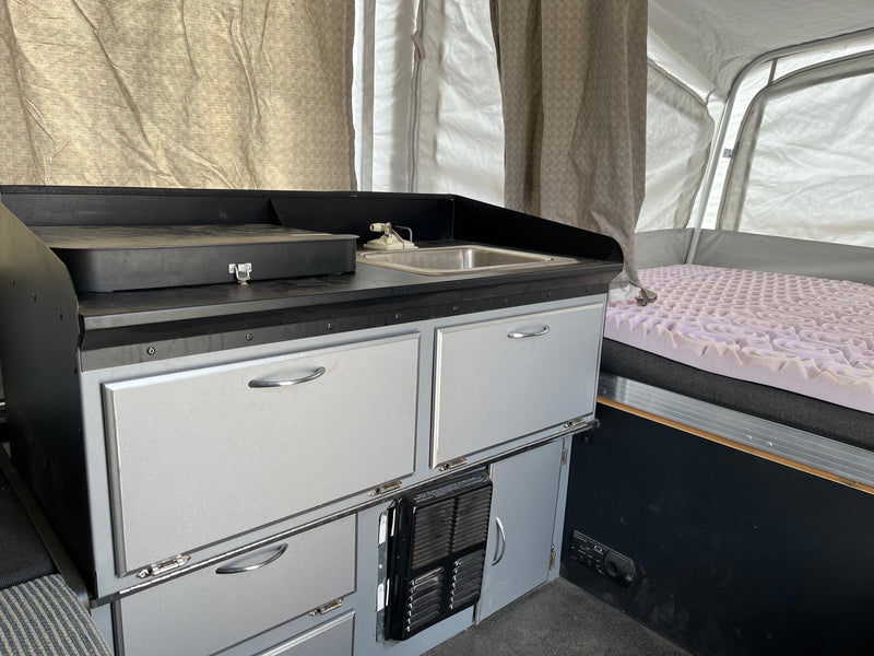 Interior of a pop-up camper RV rental: compact kitchen with a sink, storage cabinets, and a comfortable bed. — photo 6