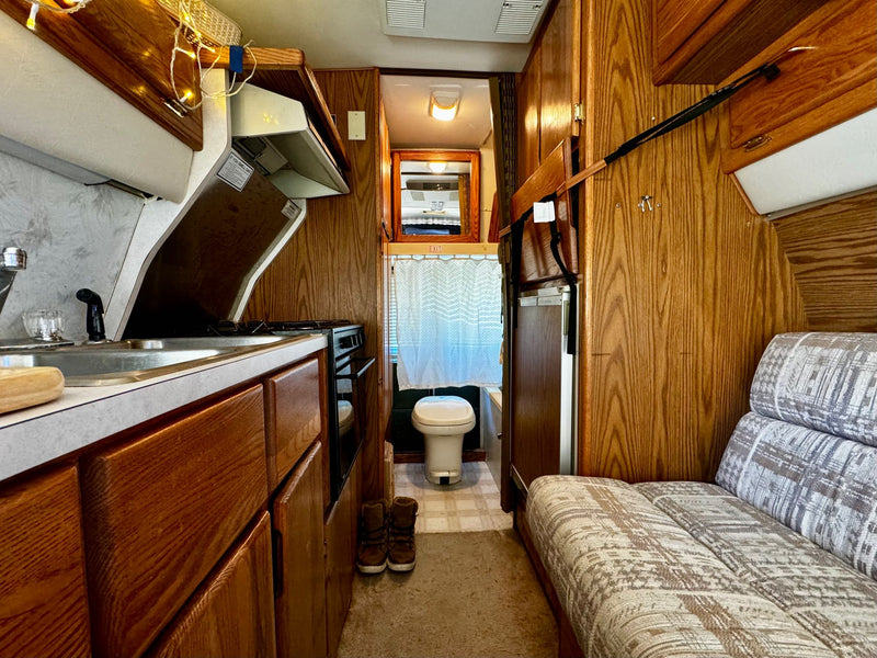  is ready for adventure! Parked at night with blue awning lights and warm interior glow.|Cozy RV rental interior featuring overhead wooden cabinets — photo 3