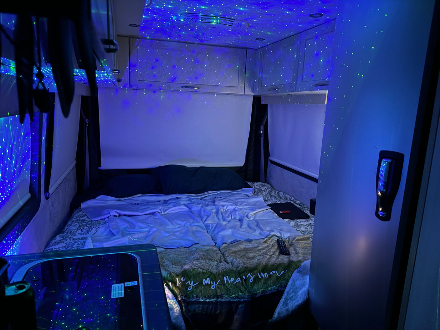 Dreamy rv rental bedroom with a galaxy of blue and green lights on the ceiling, a comfortable bed, and compact storage in this camper.