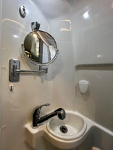 A compact bathroom in an RV rental, featuring a white sink, chrome pull-out faucet, and adjustable magnifying mirror.