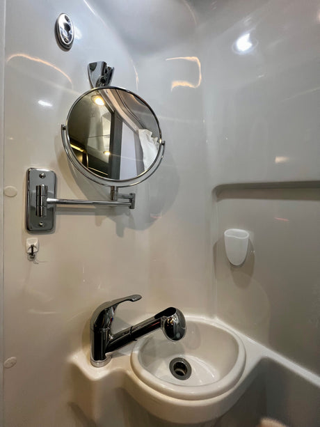 A compact bathroom in an RV rental, featuring a white sink, chrome pull-out faucet, and adjustable magnifying mirror.