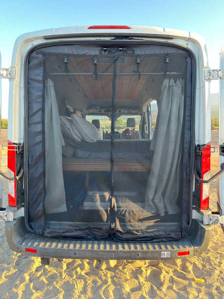 Inside an RV rental van, a rear mesh screen provides bug protection. Features include a bed and storage for comfortable travel.
