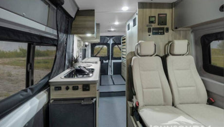 View of an RV rental interior: compact kitchen, two passenger seats, and control panels. Ready for adventure.