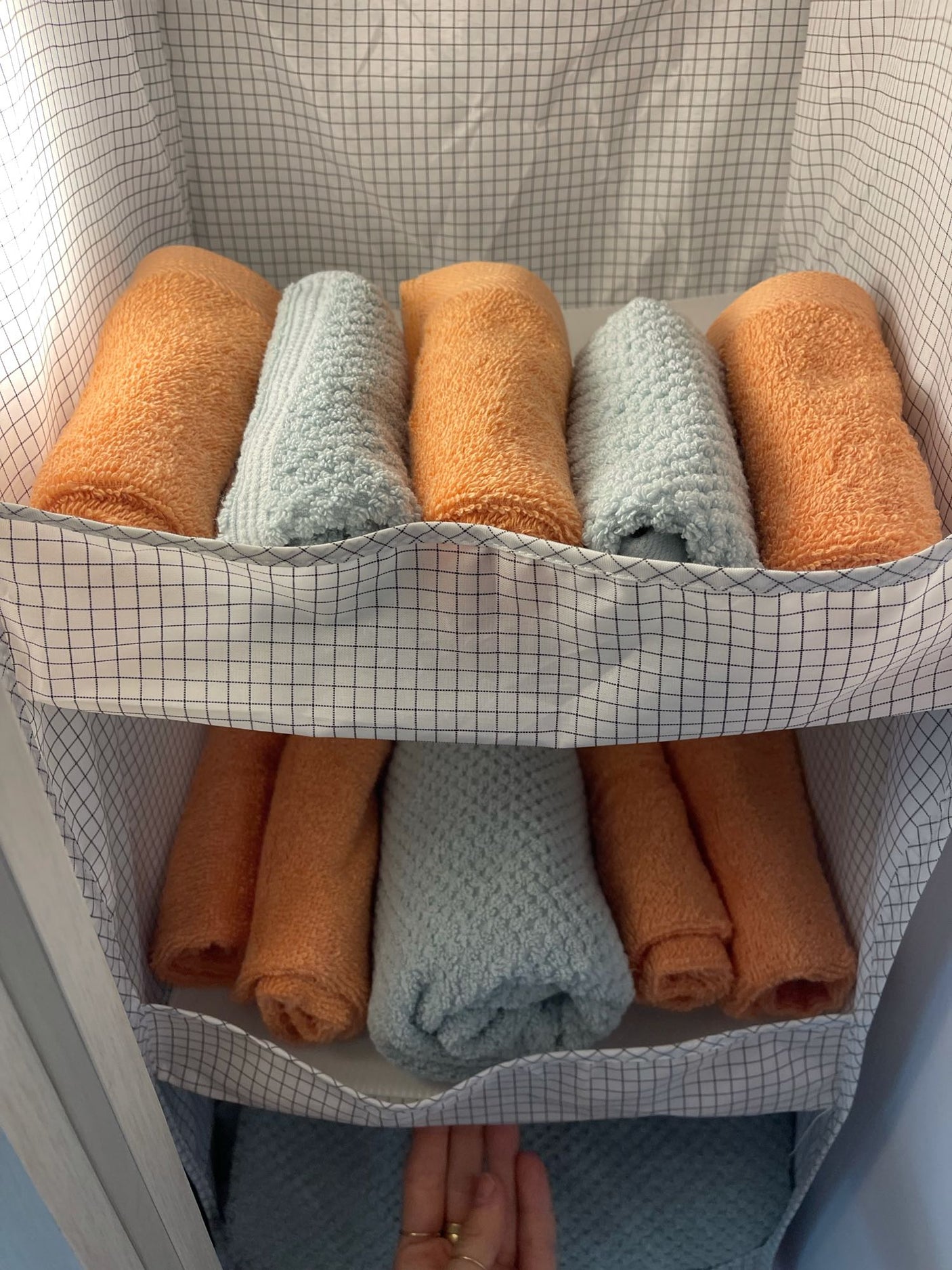 Efficient RV rental storage: Neatly rolled orange and blue towels in a checkered hanging organizer. Perfect for compact living.