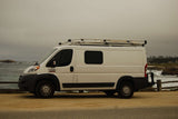 White Ram ProMaster RV rental van with roof rack parked at a scenic coastal spot by crashing ocean waves.