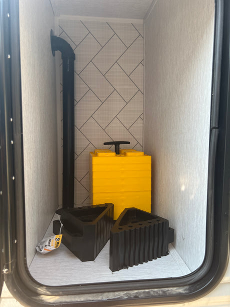 RV rental utility compartment showing yellow leveling blocks, black wheel chocks, and drain plumbing. Essential for safe setup.