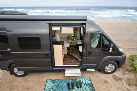 Scenic rv rental campervan parked on a sandy beach with its door open, showing a dining area and ocean views. Perfect beach vacation!