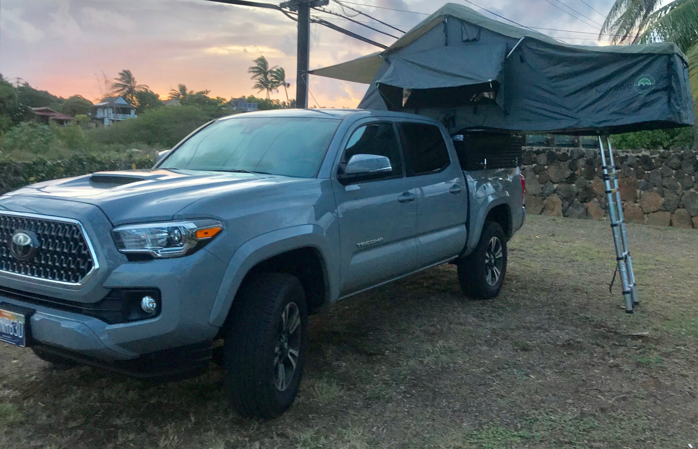 Grey Toyota Tacoma with a rooftop tent deployed for truck camping, like an RV rental adventure at sunset.