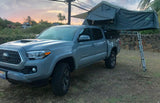 Grey Toyota Tacoma with a rooftop tent deployed for truck camping, like an RV rental adventure at sunset.
