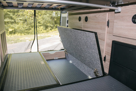 RV rental: Organized rear storage with lift-up floor, rubberized mat, and wood cabinets. Bed frame visible overhead.