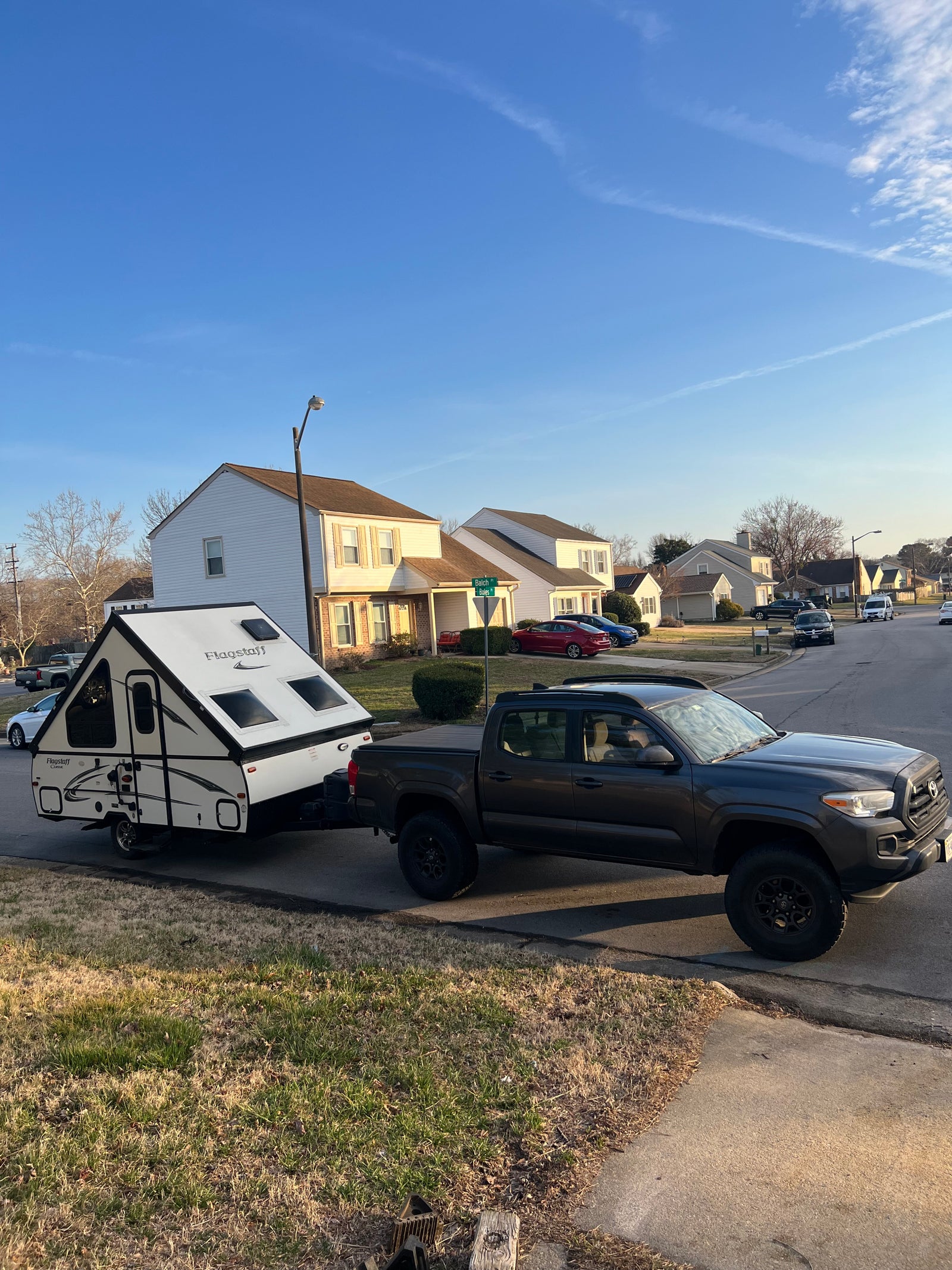 A-frame RV rental: Dark grey Tacoma pickup towing a white Flagstaff camper, set up on a suburban street, ready for camping.