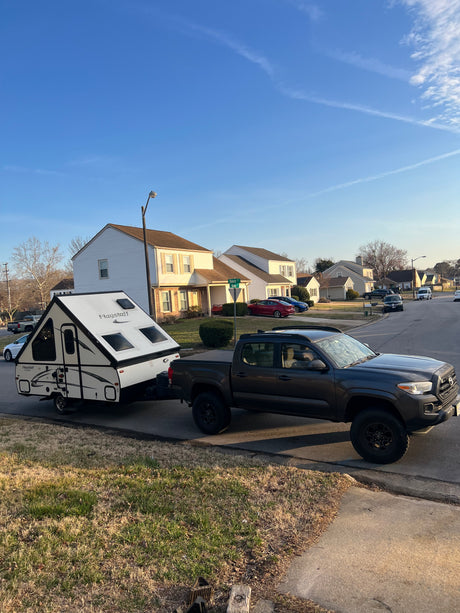 A-frame RV rental: Dark grey Tacoma pickup towing a white Flagstaff camper, set up on a suburban street, ready for camping.