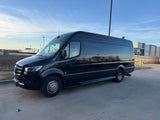 A black Mercedes-Benz Sprinter luxury van, ideal for rv rental, parked in a lot under a bright blue sky with industrial buildings behind it.