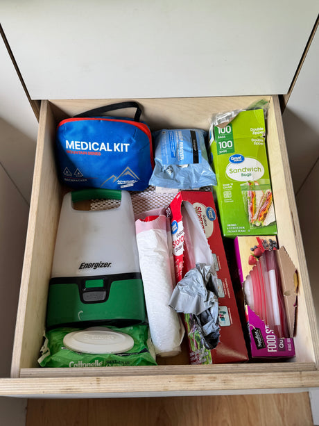 Organized rv rental drawer with travel essentials: medical kit, Energizer lantern, wipes, and various food/trash bags.