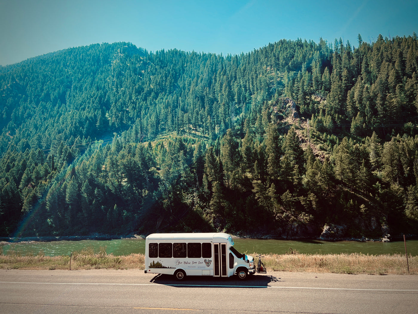 White RV rental parked by a green river and dense forest hill under clear sky. Ideal for a nature road trip. — photo 3
