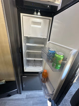 Inside an RV rental, an open Norcold refrigerator reveals compact shelves and door storage with drinks.
