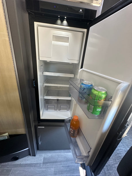 Inside an RV rental, an open Norcold refrigerator reveals compact shelves and door storage with drinks.