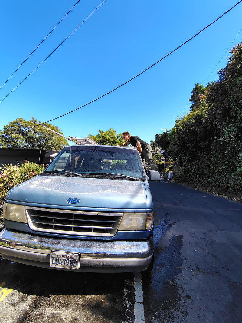 Man washing blue Ford van, prepped as an rv rental, with a ladder on roof under clear skies. — photo 7
