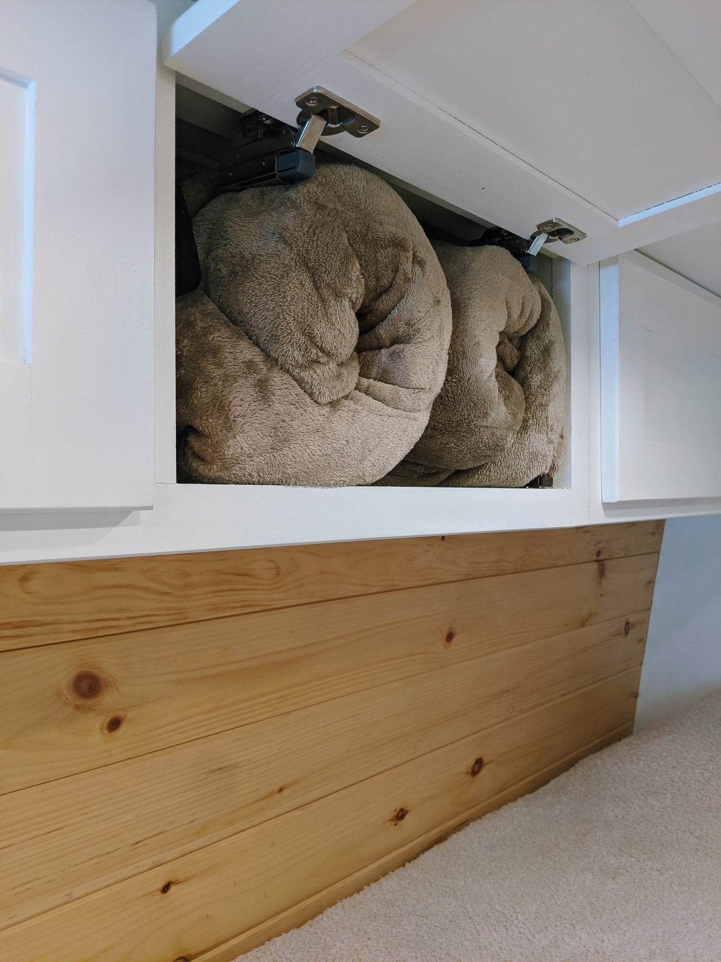 RV rental organized storage: Two soft, rolled blankets neatly inside an overhead white cabinet, above natural wood paneling.