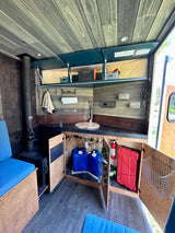 This RV rental shows a cozy camper van interior with a kitchen, wood stove, and smart storage, perfect for mobile living.