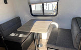 Cozy RV rental dinette interior with dark gray benches, a wooden table, and a window, ideal for camper travel.