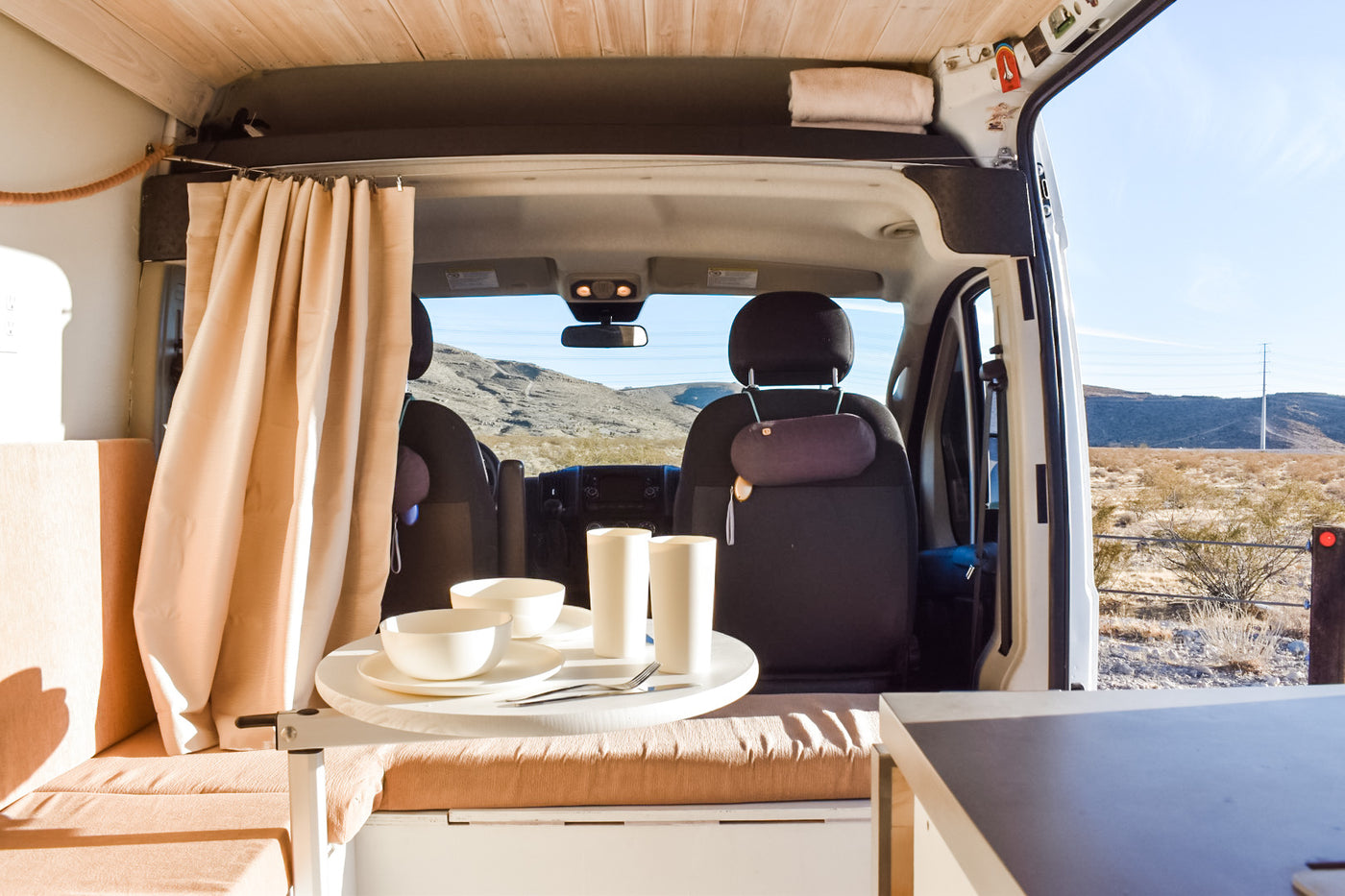 An RV rental van's cozy interior, featuring a dining table setup with desert landscape views beyond the cab. — photo 17