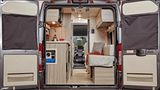 View from rear: an RV rental's inviting interior. Left: functional kitchen. Right: comfortable seating/bed. Doors open to reveal.