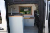Inside a spacious RV rental camper van: light blue kitchenette with sink, wood countertops, and a window overlooking nature.