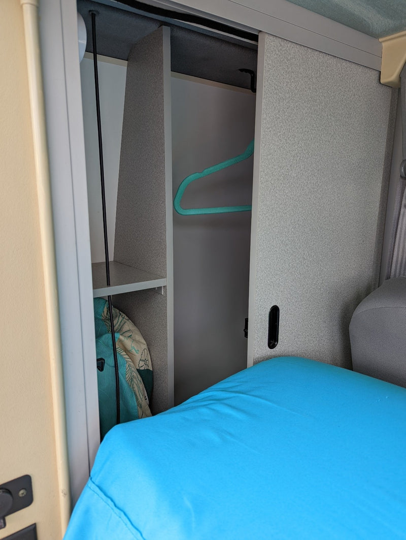 RV rental: Compact interior wardrobe with a turquoise hanger, lower shelf, and a vibrant blue bed. — photo 8