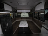 RV rental interior features a U-shaped dinette with marble table, compact kitchen, and large windows overlooking other RVs.