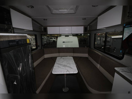 RV rental interior features a U-shaped dinette with marble table, compact kitchen, and large windows overlooking other RVs.