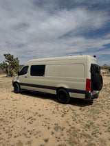 White Sprinter camper van, an RV rental, on a dirt road in the desert, with Joshua trees.