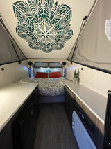 Cozy A-frame RV rental interior with a unique ceiling design, bed, and compact living space. Ideal for your next adventure.