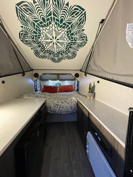 Cozy A-frame RV rental interior with a unique ceiling design, bed, and compact living space. Ideal for your next adventure.