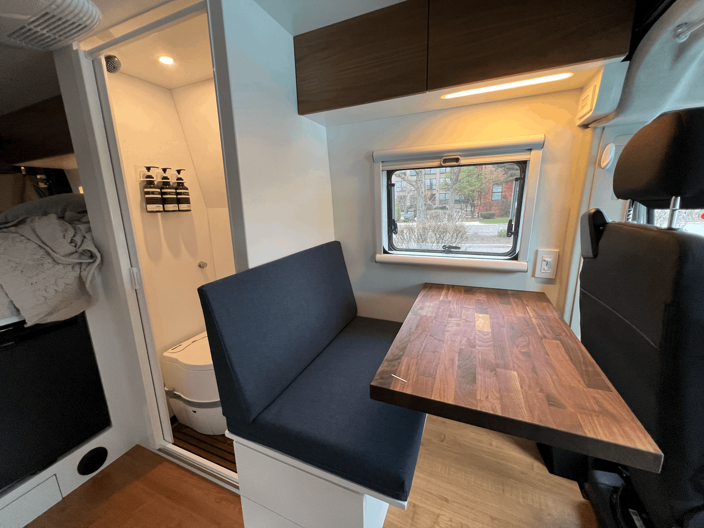 Cozy RV rental interior featuring a wooden dining table, bench seating, and compact wet bath with shower and toilet.