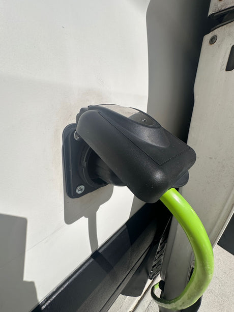 An RV rental is plugged into shore power via a bright green cable and black connector on its white exterior.