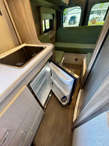 Convenient rv rental kitchenette: stovetop, open fridge, and cozy green seating inside.