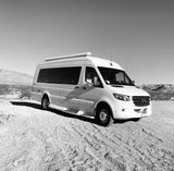 A white Mercedes-Benz Sprinter rv rental parked on a gravel road in a vast desert landscape with distant mountains.